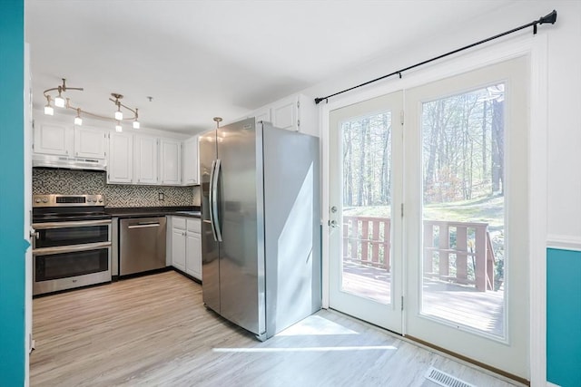 kitchen with appliances with stainless steel finishes, under cabinet range hood, white cabinets, and tasteful backsplash