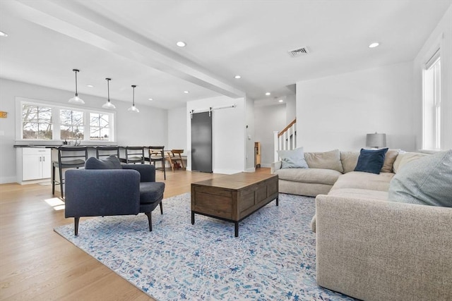 living area with a wealth of natural light, visible vents, light wood-style flooring, and a barn door