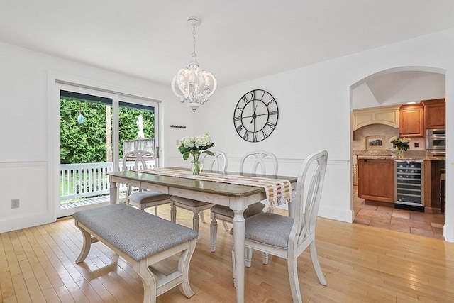 dining area with wine cooler, an inviting chandelier, arched walkways, baseboards, and light wood-style floors