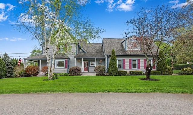 new england style home featuring roof with shingles and a front lawn
