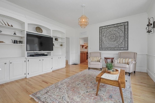 living room featuring crown molding, light wood-style flooring, and a wainscoted wall