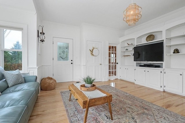living area featuring a wainscoted wall, an inviting chandelier, ornamental molding, and light wood-type flooring