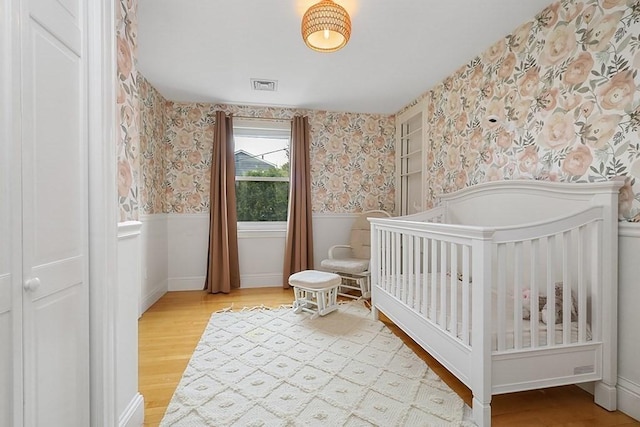 bedroom featuring visible vents, wallpapered walls, a wainscoted wall, and wood finished floors