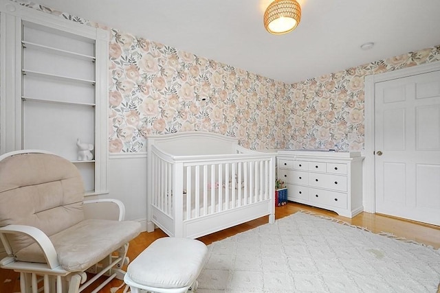 bedroom featuring a nursery area, wallpapered walls, and wood finished floors