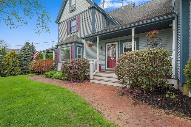 doorway to property featuring a shingled roof, a porch, and a lawn