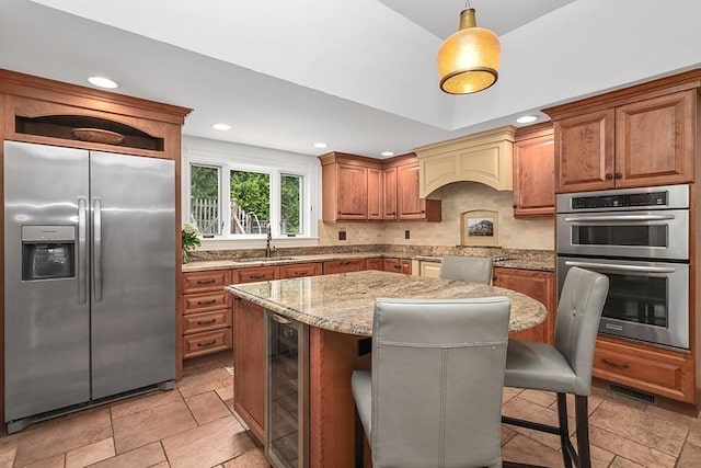 kitchen featuring light stone countertops, beverage cooler, a sink, backsplash, and appliances with stainless steel finishes
