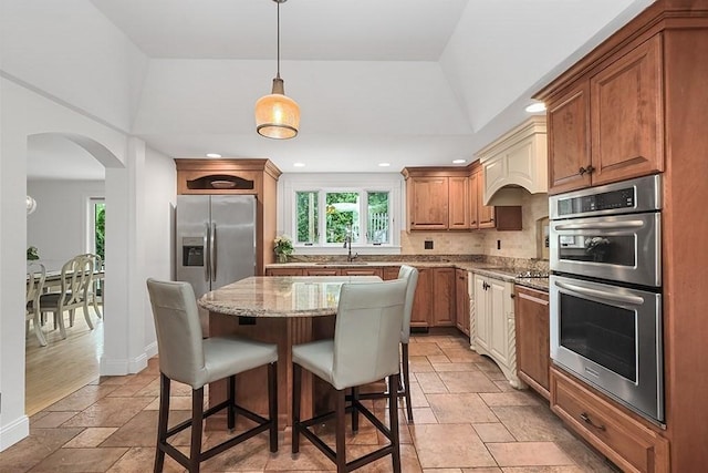 kitchen with a center island, a kitchen breakfast bar, stone tile floors, light stone countertops, and appliances with stainless steel finishes