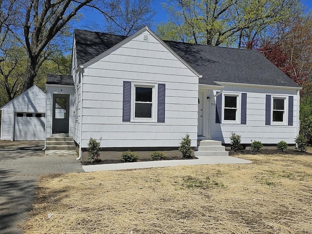 view of front facade with an outbuilding, a garage, aphalt driveway, a shingled roof, and entry steps