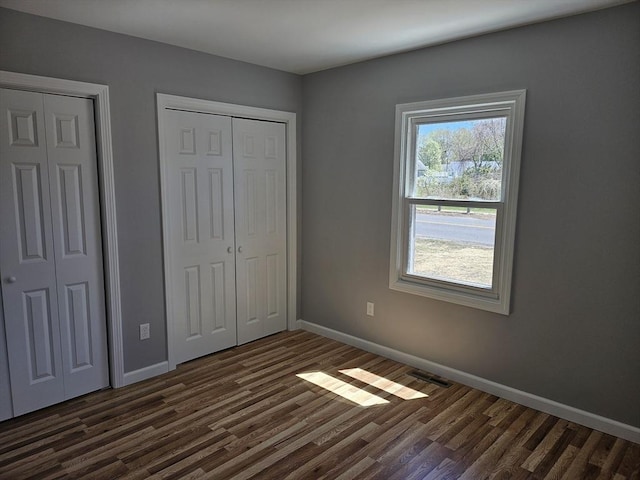 unfurnished bedroom featuring baseboards, dark wood-style flooring, and two closets