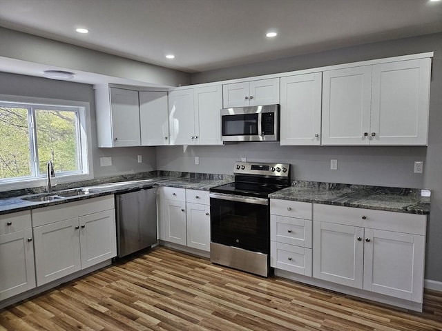 kitchen with wood finished floors, recessed lighting, white cabinets, a sink, and appliances with stainless steel finishes