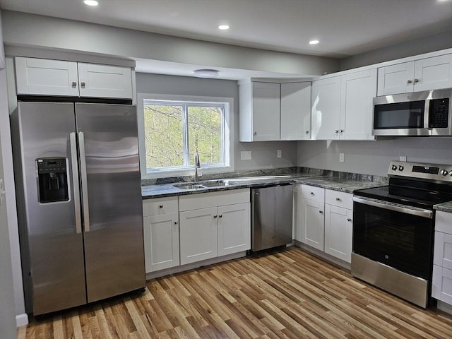 kitchen featuring white cabinets, stainless steel appliances, a sink, and light wood-type flooring