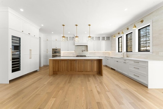 kitchen featuring white cabinetry, decorative light fixtures, light hardwood / wood-style flooring, and a spacious island