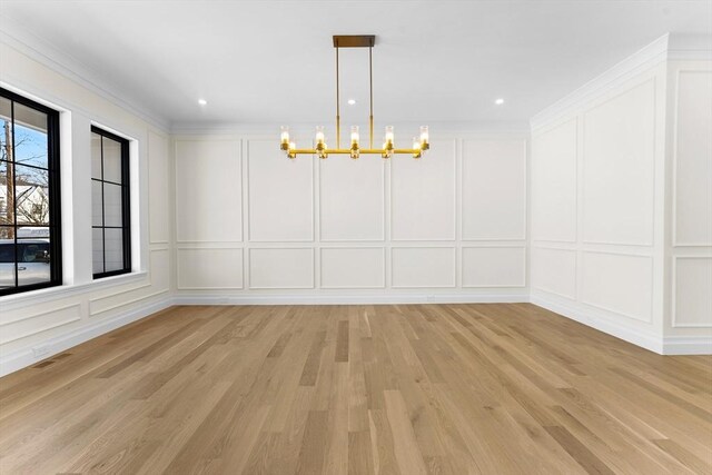 unfurnished dining area with a notable chandelier, ornamental molding, and light wood-type flooring