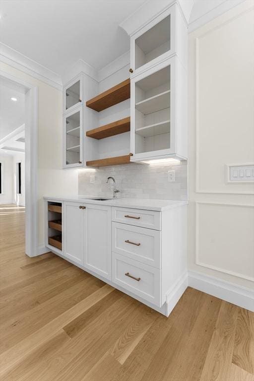 kitchen featuring sink, ornamental molding, light hardwood / wood-style floors, decorative backsplash, and white cabinets