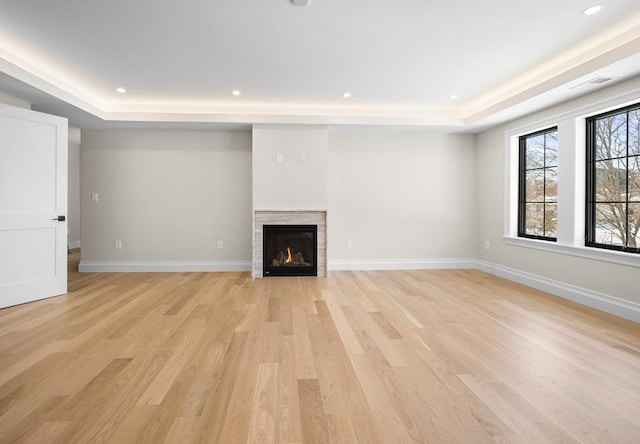 unfurnished living room with light hardwood / wood-style flooring and a tray ceiling