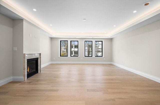 unfurnished living room featuring a raised ceiling, a premium fireplace, and light hardwood / wood-style floors