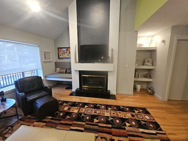 living room featuring a tiled fireplace, hardwood / wood-style flooring, vaulted ceiling, and built in shelves