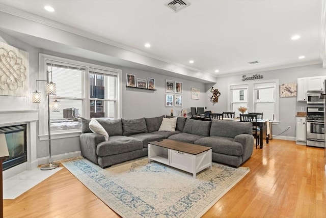 living room featuring light wood-style flooring, a tile fireplace, visible vents, and crown molding