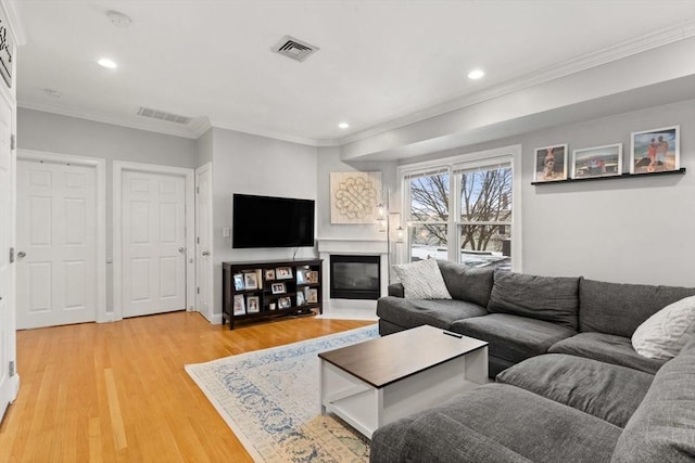 living area with crown molding, recessed lighting, visible vents, light wood-style flooring, and a glass covered fireplace