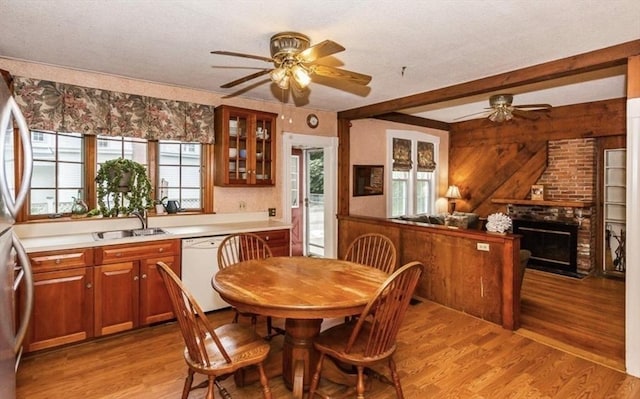 dining room with a ceiling fan, a fireplace, beamed ceiling, and light wood finished floors