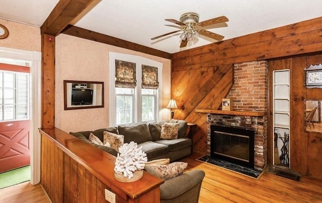 living area featuring wood walls, a fireplace, wood finished floors, a ceiling fan, and beamed ceiling