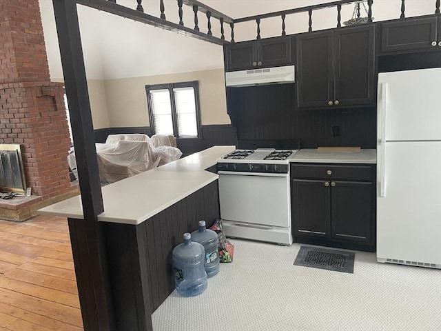 kitchen with dark cabinets, white appliances, light countertops, and under cabinet range hood