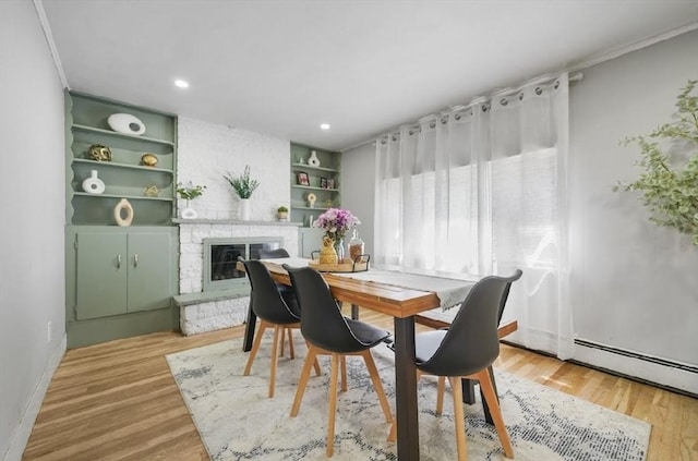 dining room with a stone fireplace, baseboards, wood finished floors, built in shelves, and crown molding