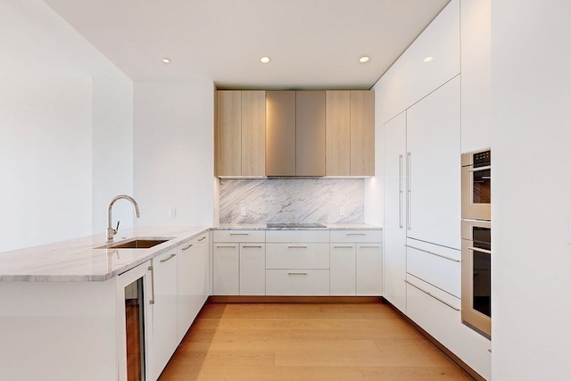 kitchen with black electric cooktop, sink, light hardwood / wood-style floors, kitchen peninsula, and backsplash