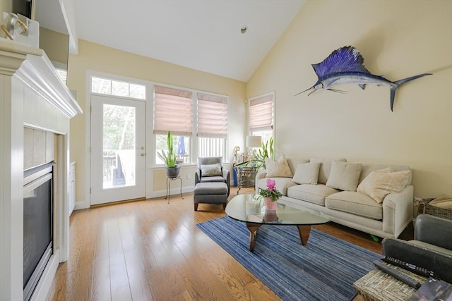 living room featuring a tiled fireplace, high vaulted ceiling, and light hardwood / wood-style flooring