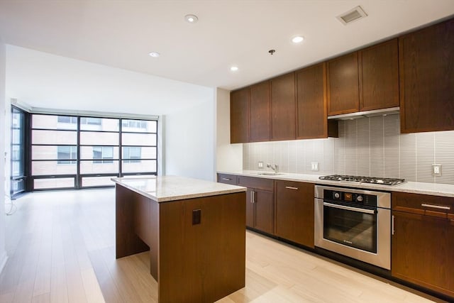 kitchen with light wood finished floors, appliances with stainless steel finishes, backsplash, a center island, and a sink