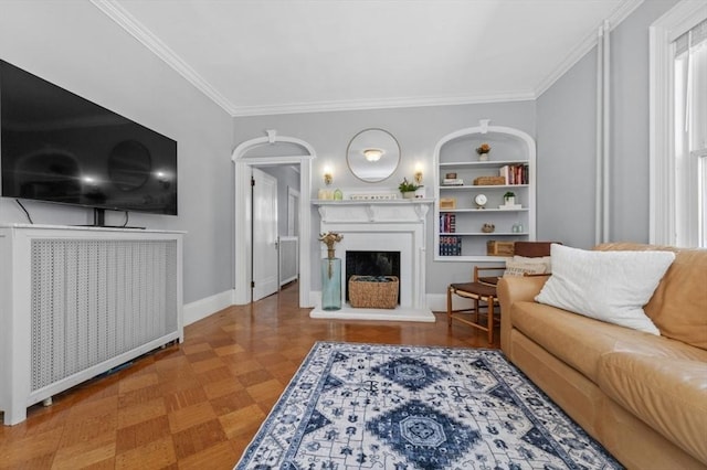 living area with crown molding, a fireplace with raised hearth, baseboards, and built in shelves