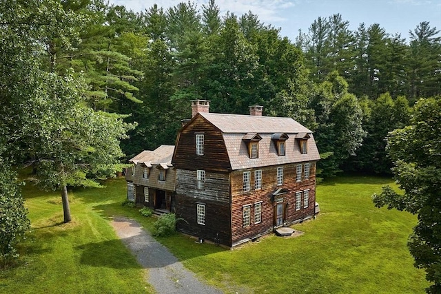 exterior space featuring aphalt driveway, a gambrel roof, a yard, and a chimney