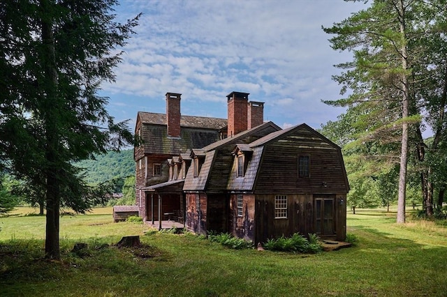 view of home's exterior featuring a gambrel roof, a lawn, and a chimney