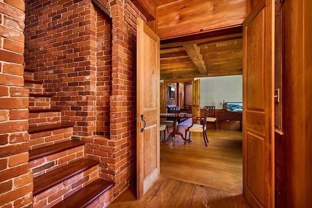 hallway with beamed ceiling, wood-type flooring, wooden ceiling, and brick wall