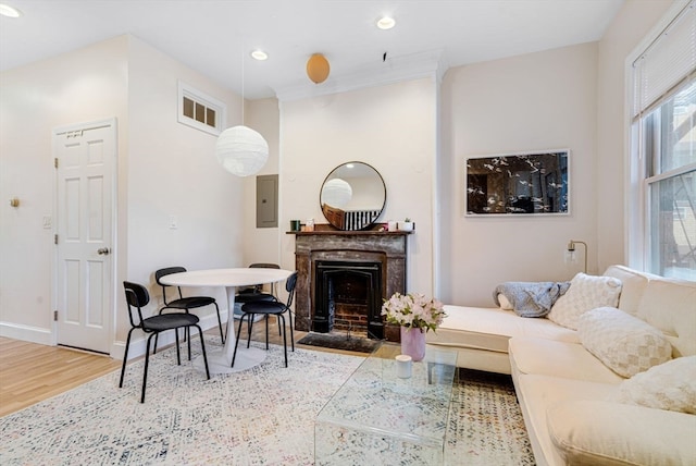 living room featuring electric panel, a high end fireplace, light hardwood / wood-style floors, and crown molding