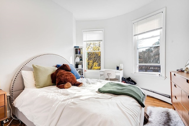 bedroom featuring light wood-type flooring, multiple windows, and a baseboard heating unit