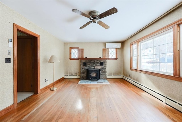 unfurnished living room featuring a baseboard heating unit, wood-type flooring, an AC wall unit, and a wood stove