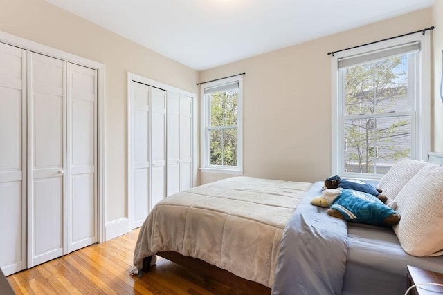 bedroom featuring light wood-style floors, baseboards, and two closets