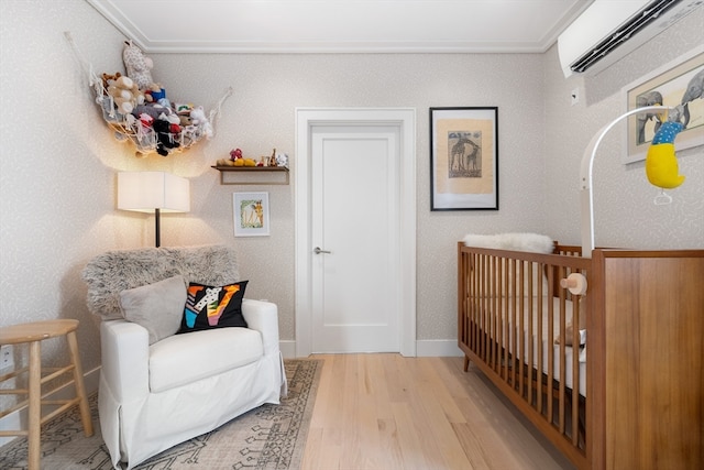 bedroom with light wood-type flooring, a nursery area, and a wall mounted air conditioner