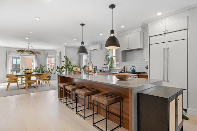 kitchen featuring light wood-type flooring, white cabinets, a wall mounted air conditioner, and a kitchen island with sink