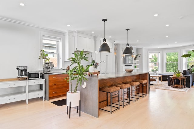 kitchen with white cabinetry, light hardwood / wood-style flooring, decorative light fixtures, and a kitchen breakfast bar