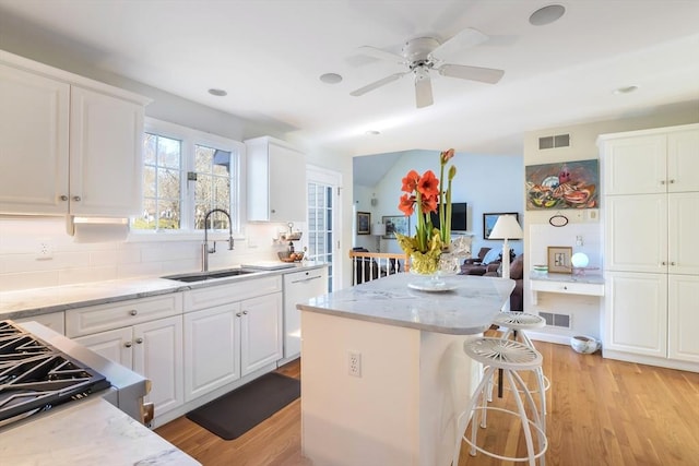 kitchen with backsplash, white dishwasher, a kitchen island, white cabinets, and sink