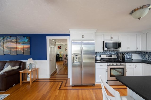 29 Wituwamat Rd, Weymouth, MA 02191 - kitchen with appliances with stainless steel finishes, dark countertops, white cabinetry, tasteful backsplash, and a wainscoted wall