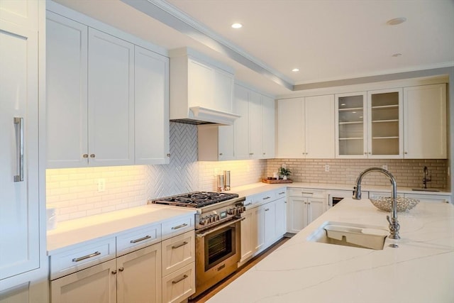 128 Elm St Unit 210, Cohasset, MA 02025 - kitchen with high end stainless steel range, glass insert cabinets, light stone countertops, white cabinets, and ornamental molding