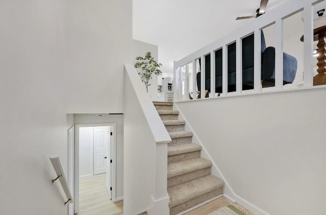 stairs featuring a ceiling fan, a high ceiling, wood finished floors, and baseboards