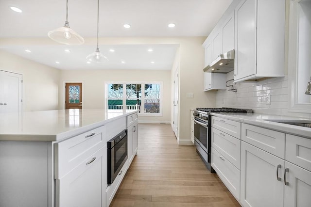 kitchen featuring white cabinetry, black microwave, high end stainless steel range oven, pendant lighting, and light hardwood / wood-style floors