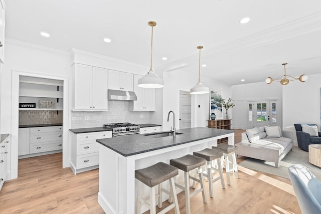 kitchen featuring a kitchen breakfast bar, light hardwood / wood-style flooring, stainless steel stove, a center island with sink, and pendant lighting