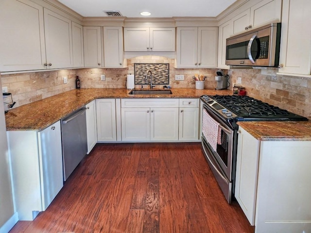 kitchen featuring dark wood-type flooring, sink, decorative backsplash, dark stone countertops, and appliances with stainless steel finishes