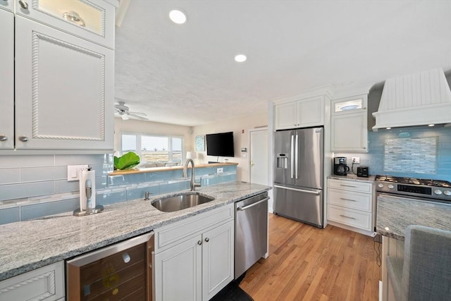 kitchen featuring premium range hood, beverage cooler, appliances with stainless steel finishes, white cabinetry, and a sink