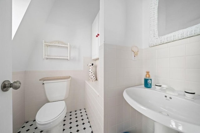 bathroom featuring a wainscoted wall, toilet, tile walls, and a sink